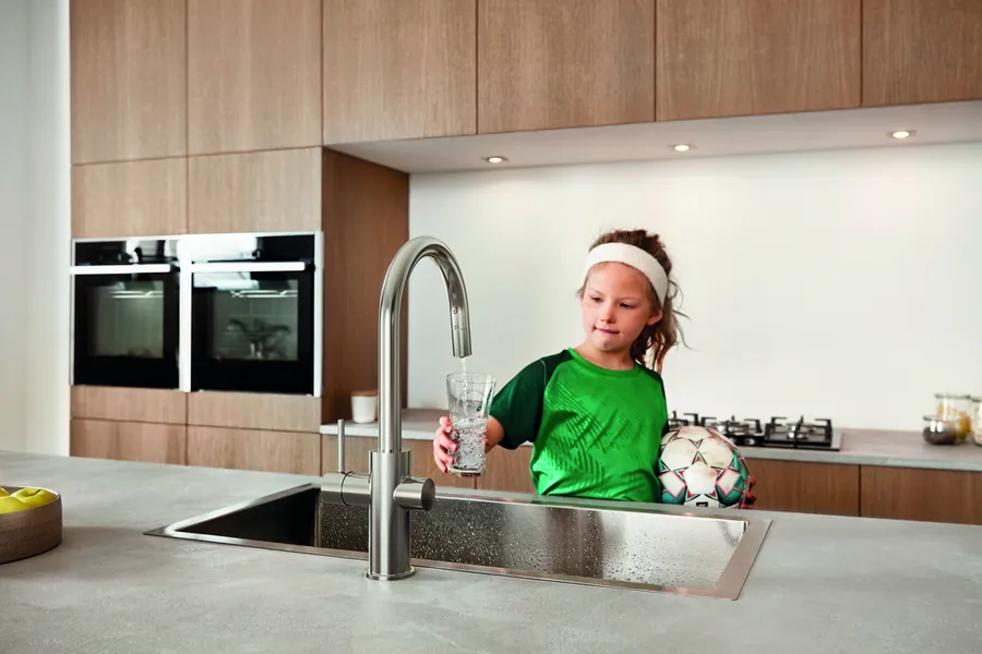 Mädchen mit Fußball füllt ein Glas an der Küchenarmatur GROHE Blue Home in Supersteel